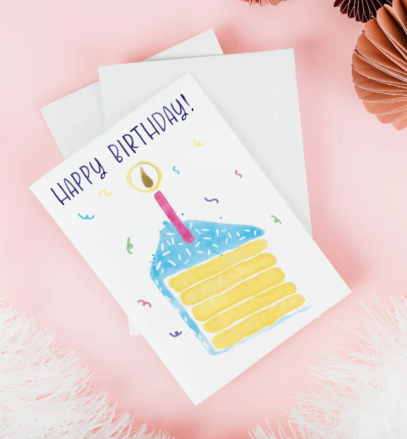 Hand-painted birthday card photographed on pink, the embedded gold bar forming the candle flame above a slice of layer cake