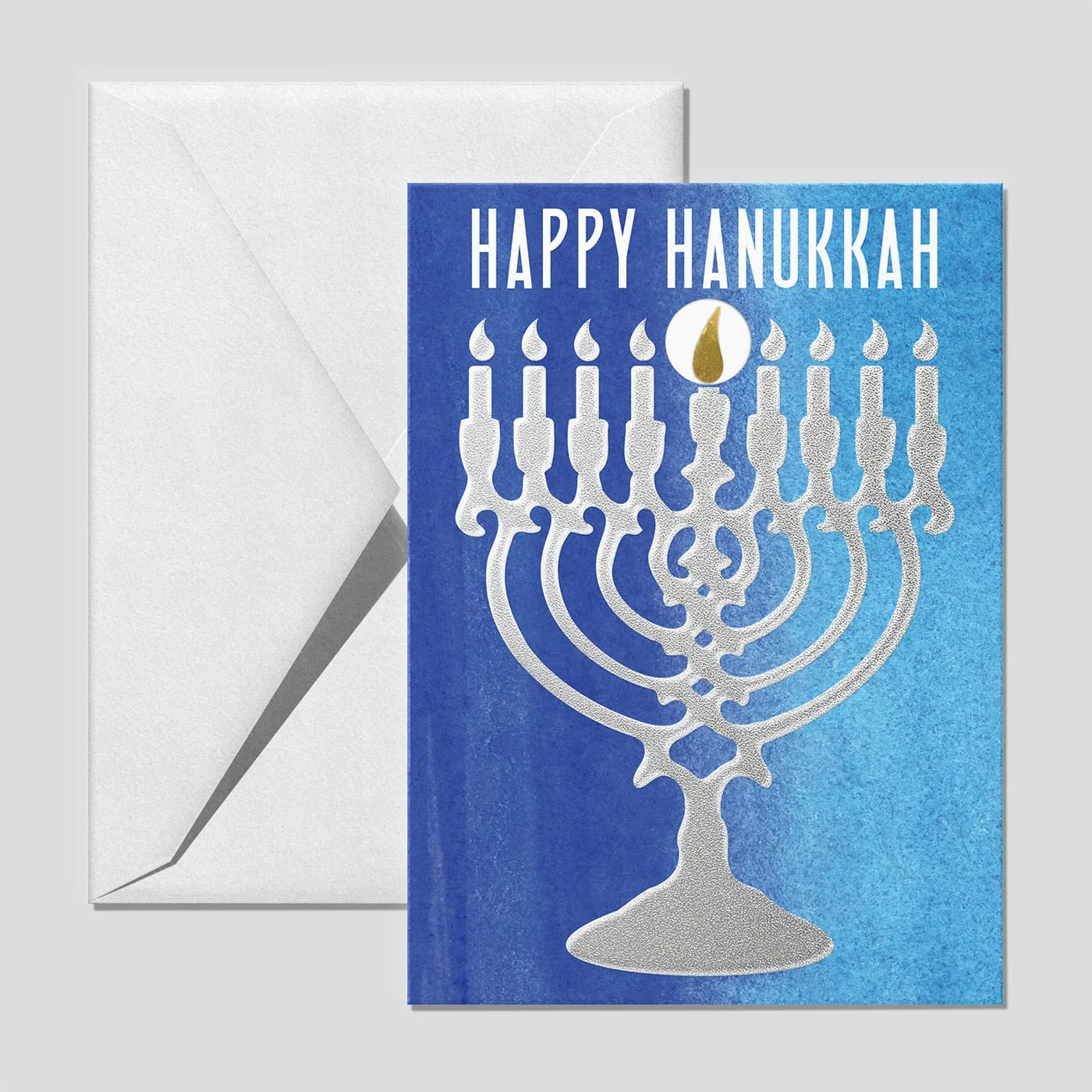 Hanukkah card with a silver textured menorah on a blue wash, the gold bar forming the shamash flame