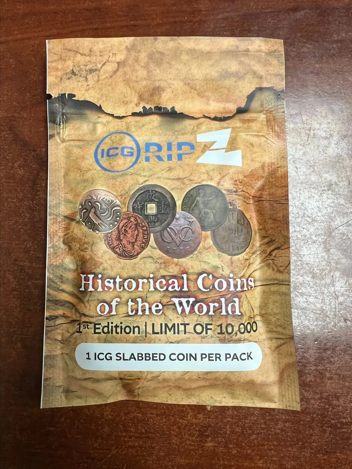 Front of a mystery coin pack, a fan of world coins on a scorched parchment pouch with an edition limit